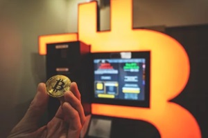 bitcoin gold coin held in hand next to Bitcoin ATM